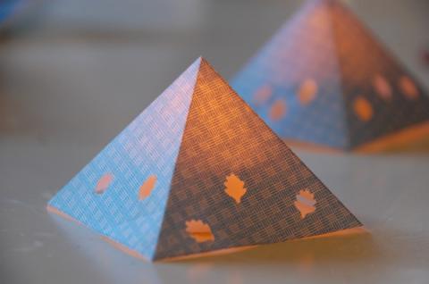 Picture of a paper pyramid with leaf cutouts. Candle is glowing inside the pyramid.